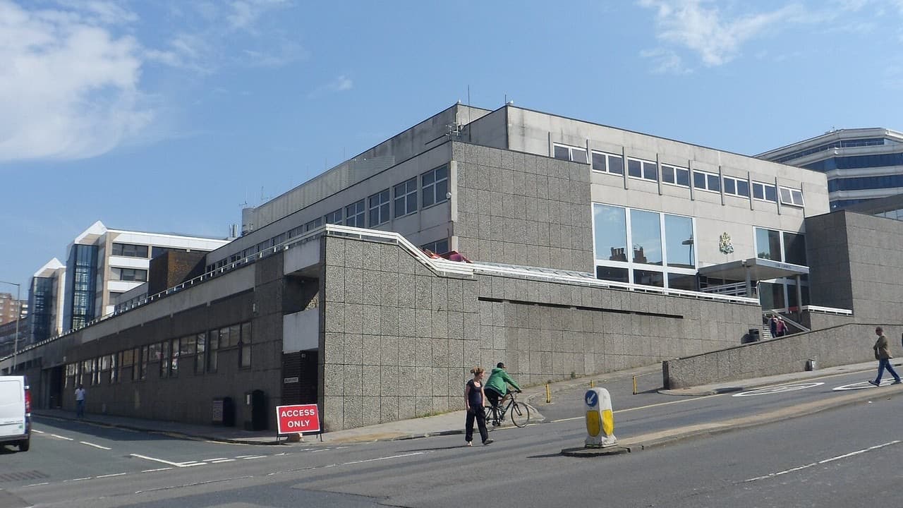 The grey stone and glass front of Brighton Law Courts with a cyclist and pedestrians passing on Edward Street
