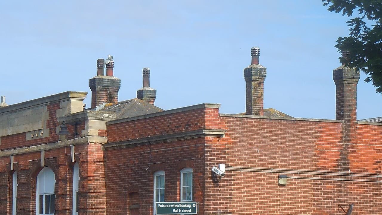 Red brick Victorian station building at Worthing railway station with arched windows and tall chimneys under a blue sky