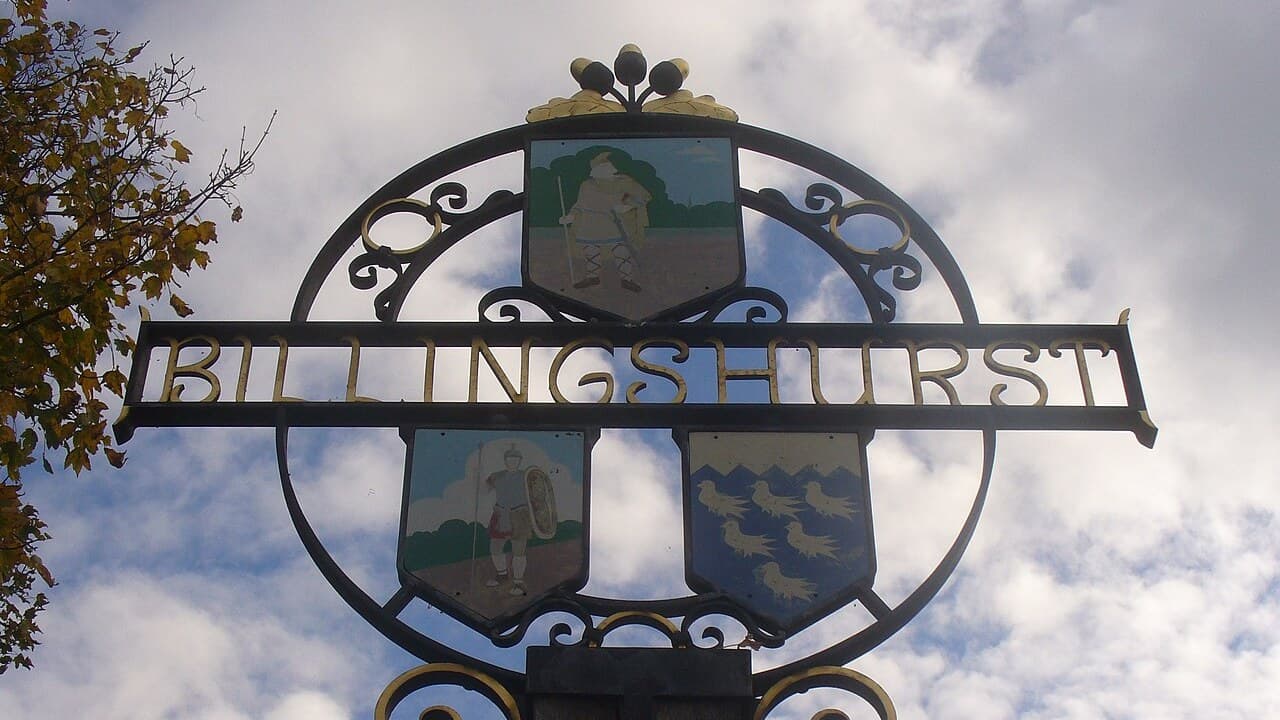 The Billingshurst village sign in West Sussex, showing three painted shields under a cloudy sky