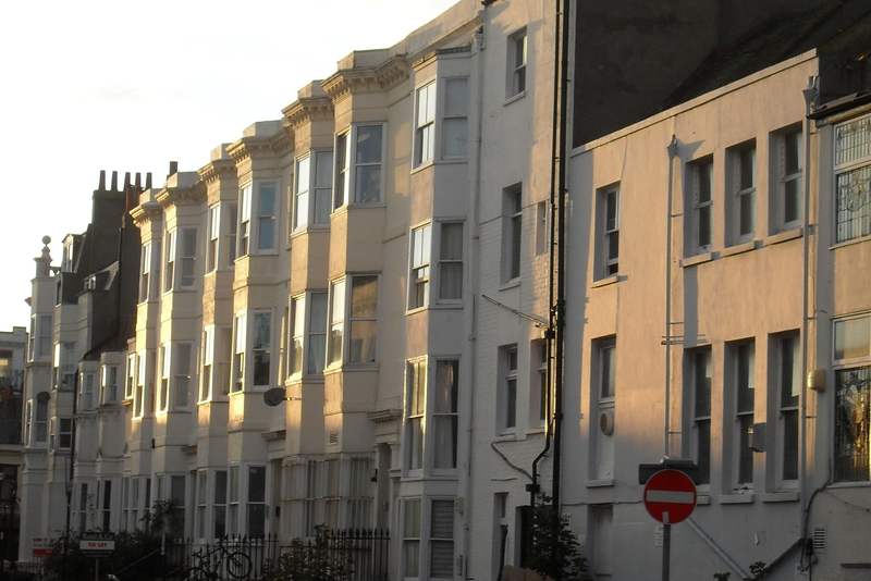 The north side of Clarence Square in Brighton, a terrace of white stucco bay-fronted houses, with the rear of the Western Road site behind