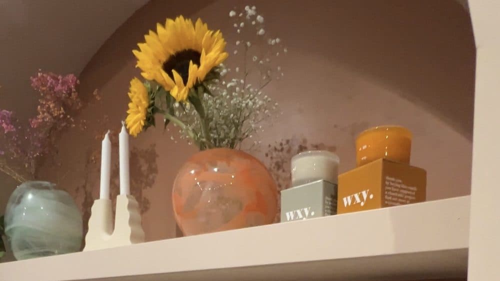 A shelf alcove inside No.64 with a vase of sunflowers, white candlesticks and boxed scented candles