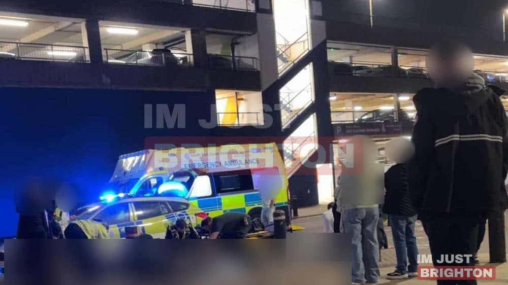 Ambulance and police vehicles at night beside a multi-storey car park at Brighton Marina, with faces blurred