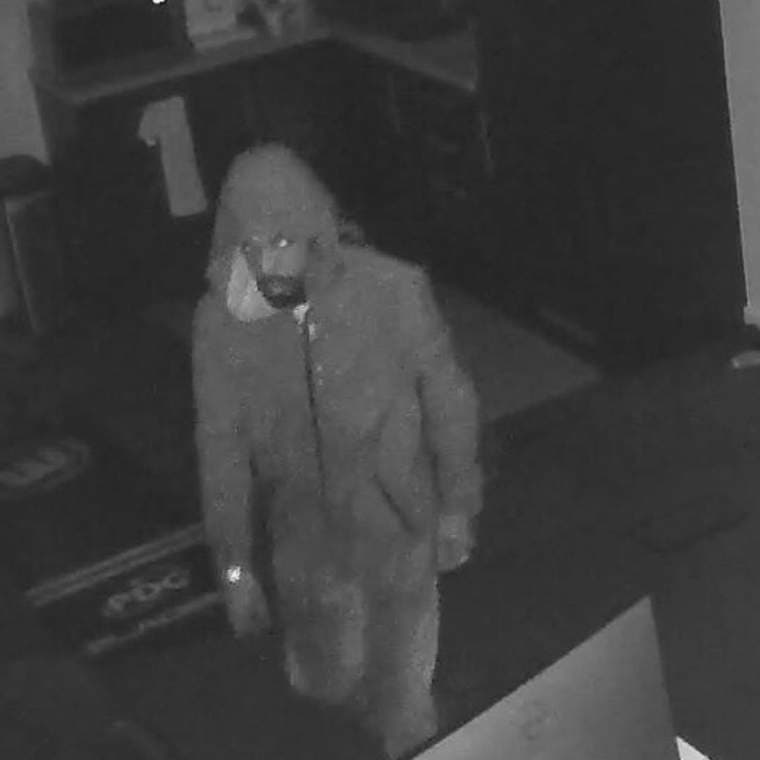 Black and white CCTV style image of a man in a hooded top standing in a dark room, released by Sussex Police