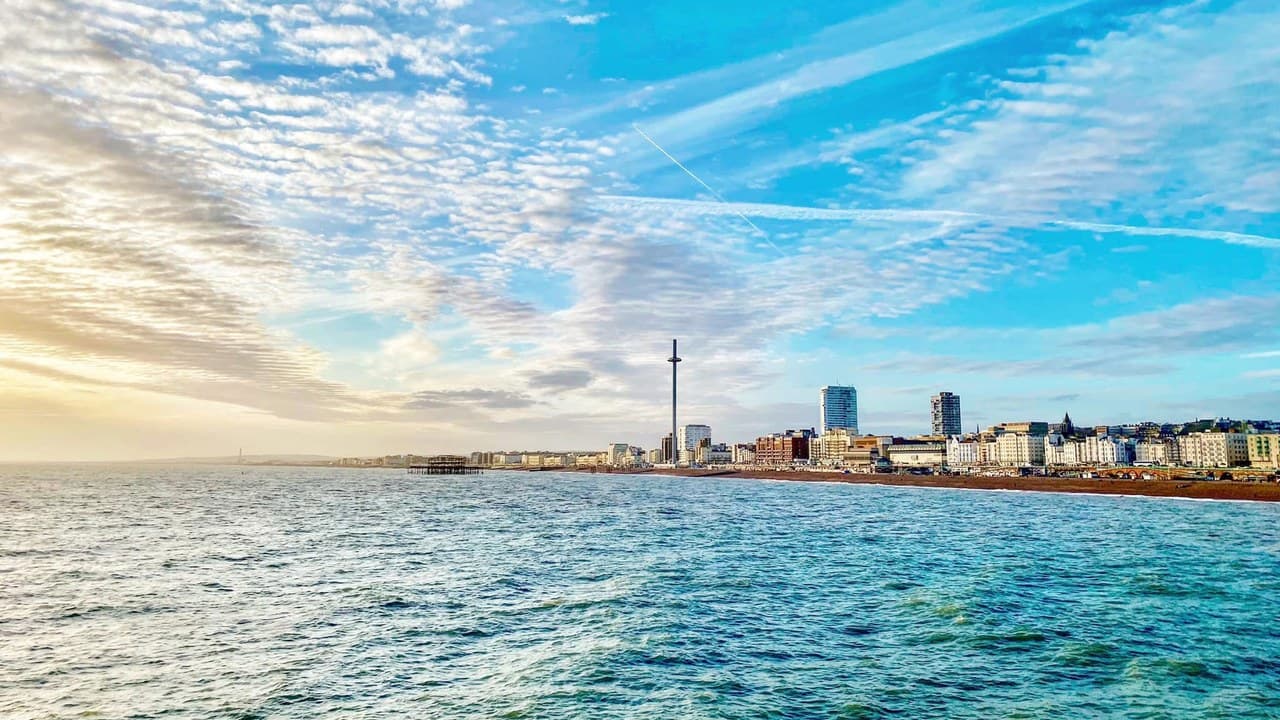 Brighton's seafront from the sea, with the i360 and the city skyline under a bright sunset sky.