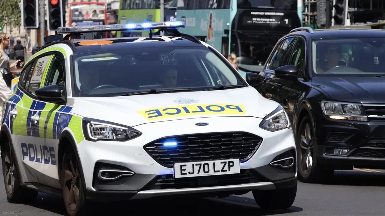 A white Sussex Police patrol car with blue lights flashing driving along a busy city street
