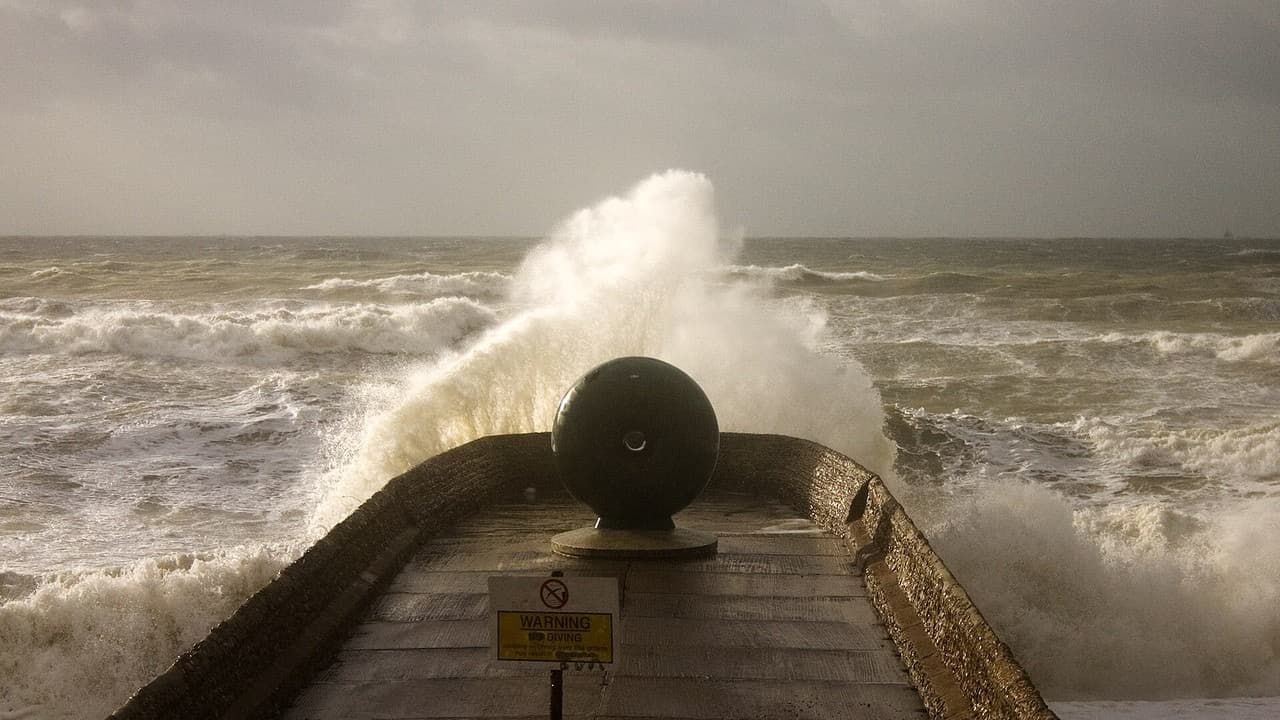 A huge wave breaking over the end of a seafront groyne at Brighton under a dark stormy sky