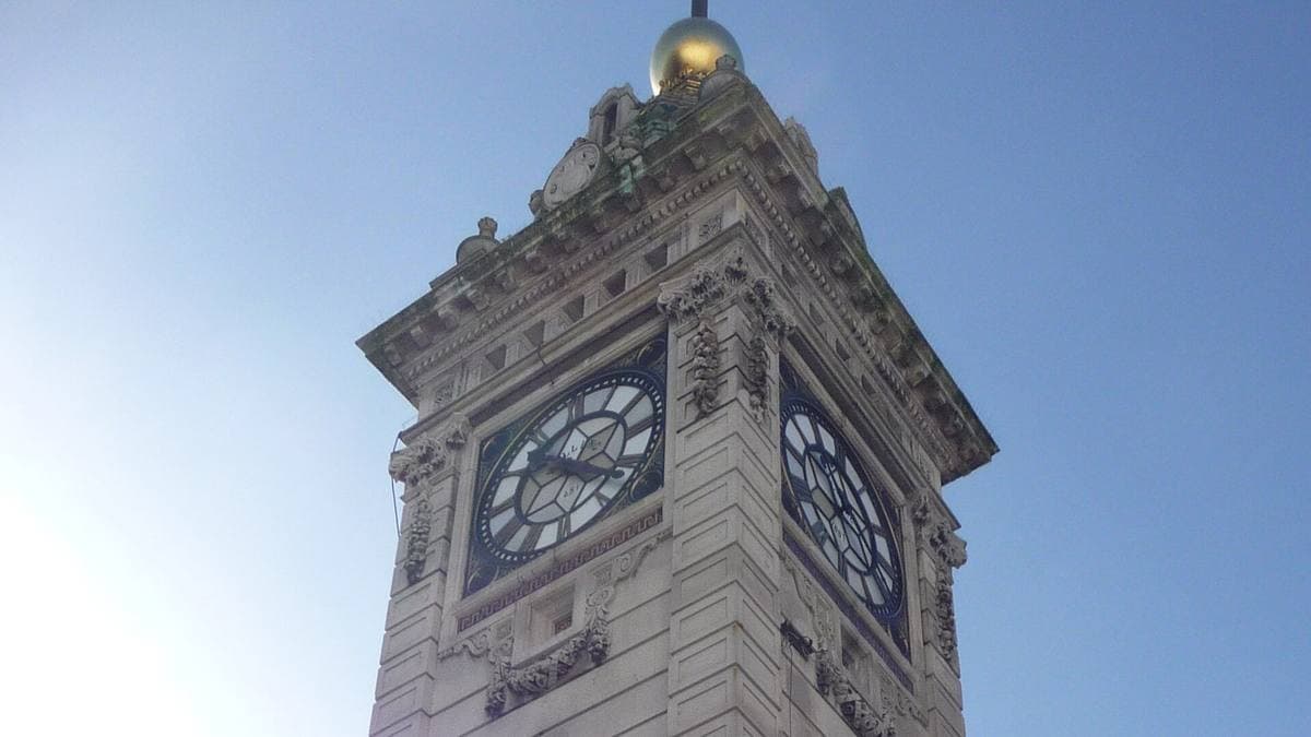 The Clock Tower in Brighton seen from below, its clock faces and gold ball against a blue sky