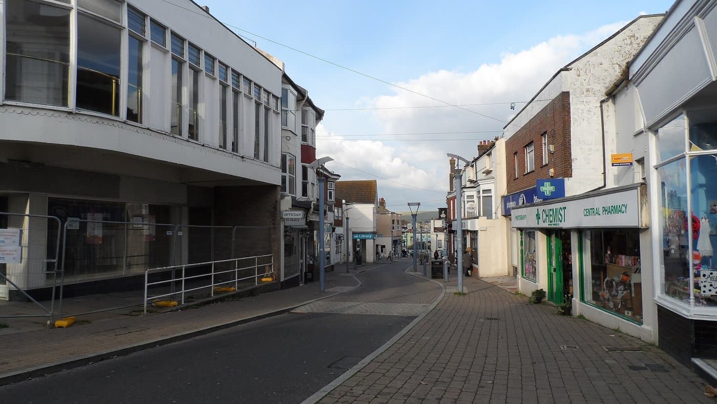 A quiet shopping street in Newhaven town centre with a pharmacy on the right and a paved pedestrian area