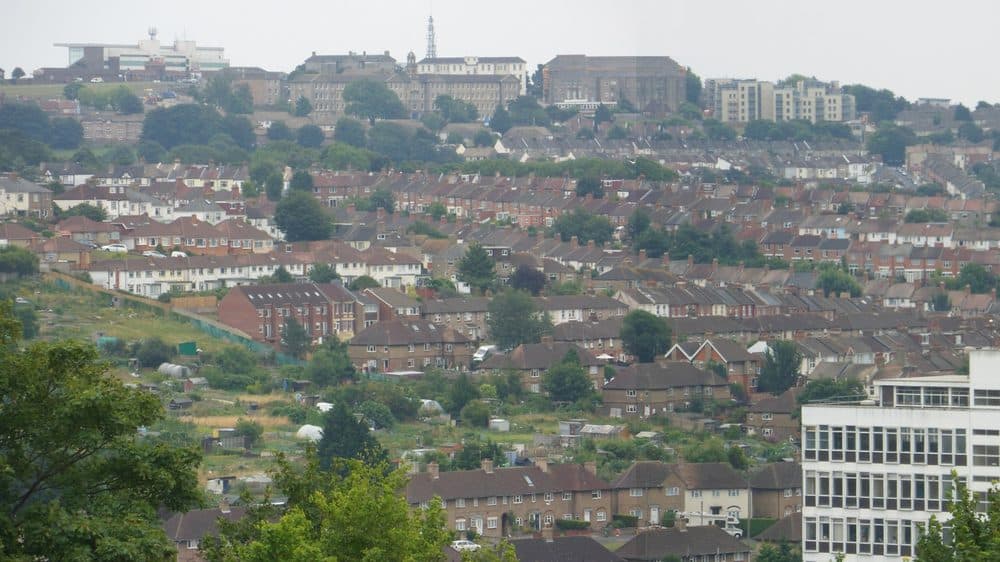 Rows of terraced and semi-detached houses on a Brighton hillside, with trees, allotments and a hospital building on the skyline