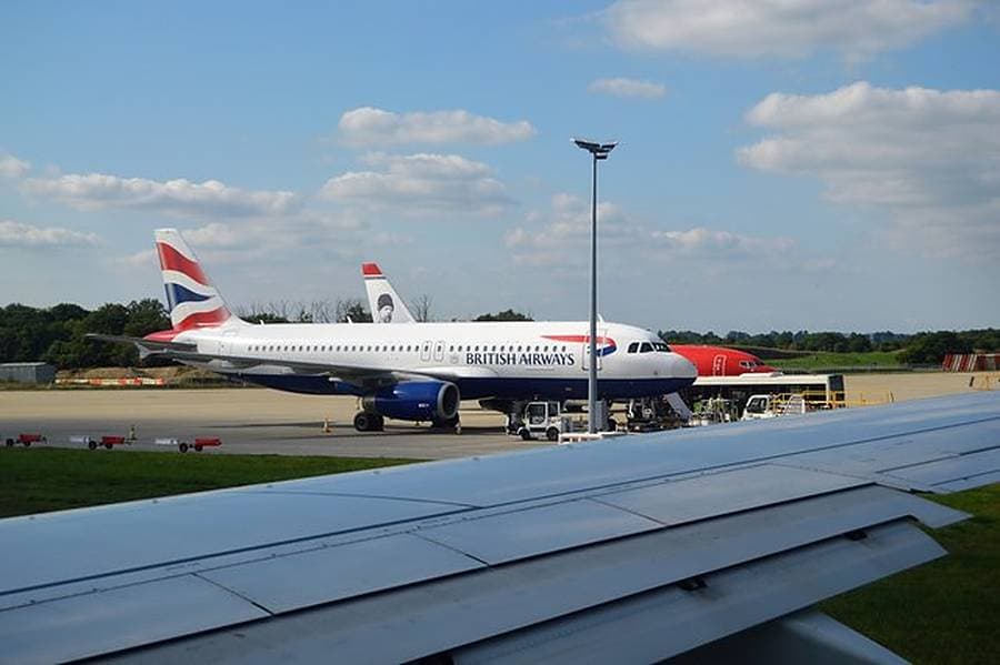 A British Airways Airbus parked at a stand at Gatwick Airport with a wing in the foreground and a blue sky above