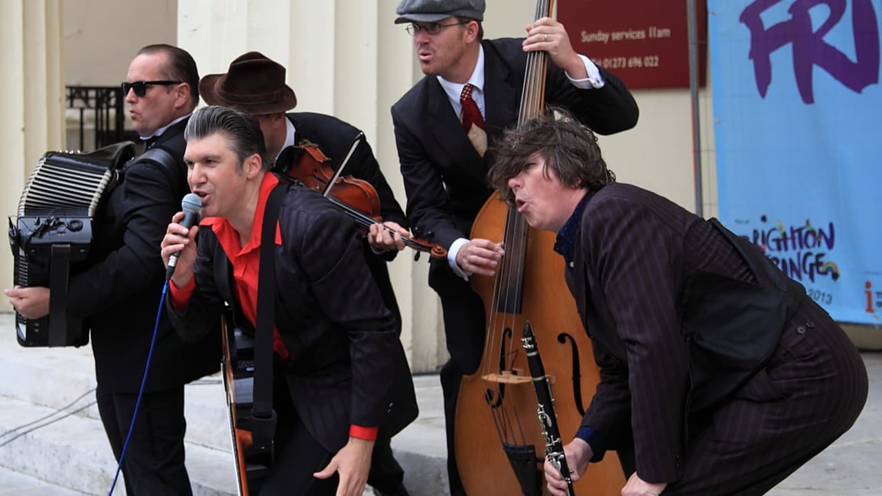 Five musicians in dark suits playing accordion, violin, double bass, guitar and clarinet on steps beside a Brighton Fringe banner