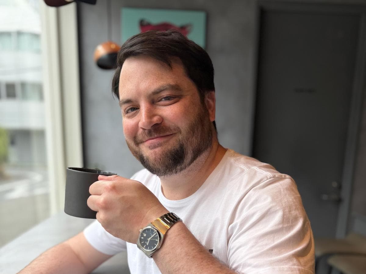 Erik Selby smiling and holding a dark mug beside a window