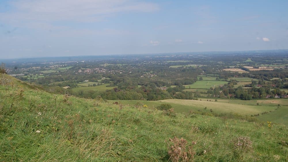 A view over the Sussex countryside from a grassy hillside on the South Downs, with fields, woods and villages stretching into the distance