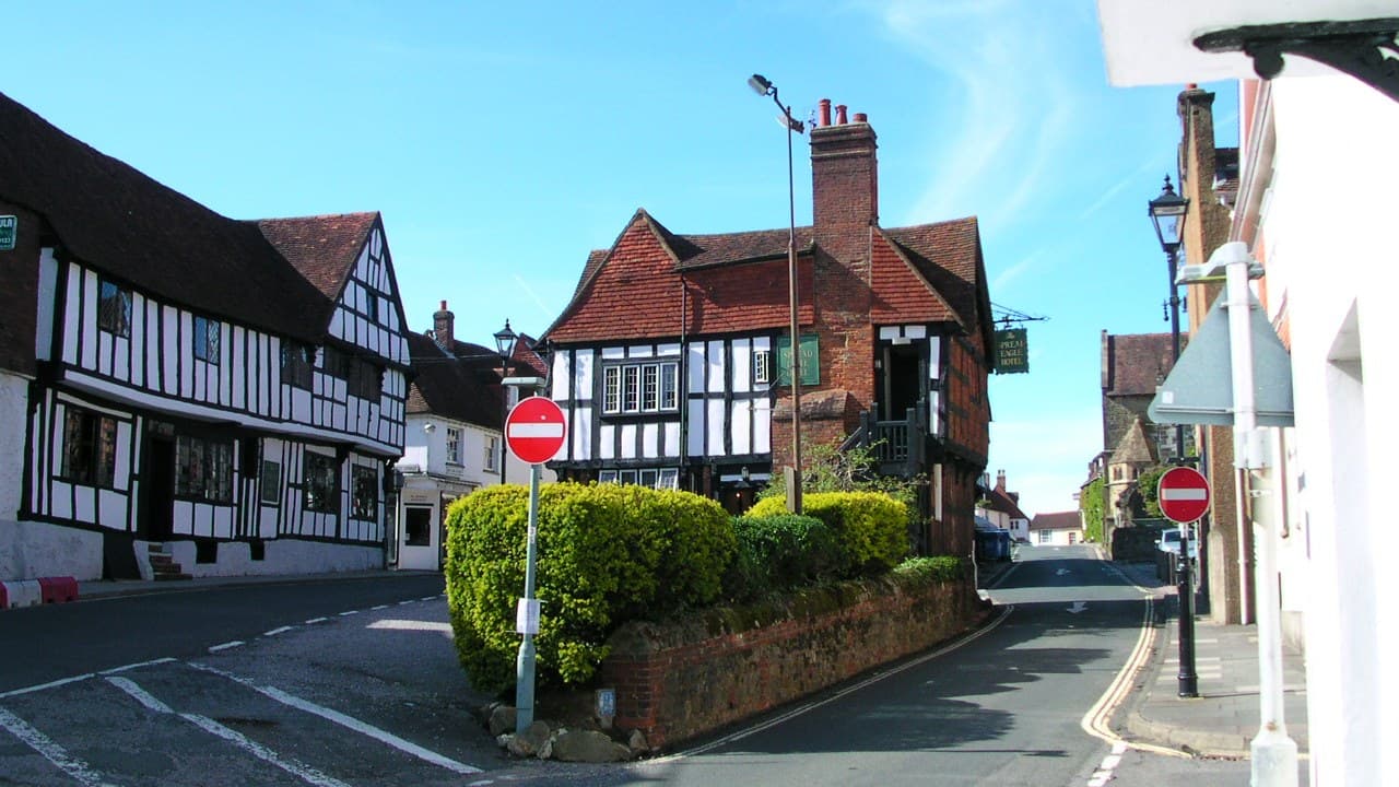 A Midhurst street with black and white timbered buildings, a red brick corner building and a blue sky