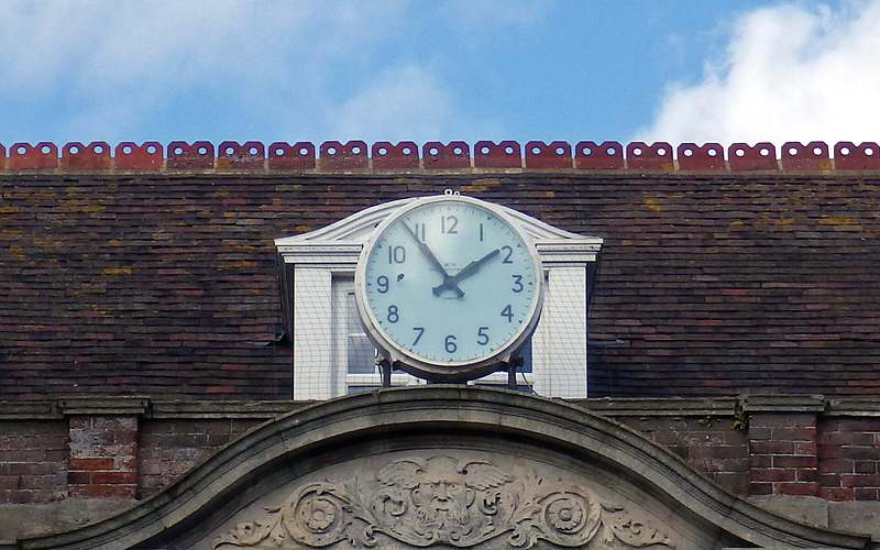The clock on the front of Bexhill Town Hall above a carved stone pediment with a blue sky behind