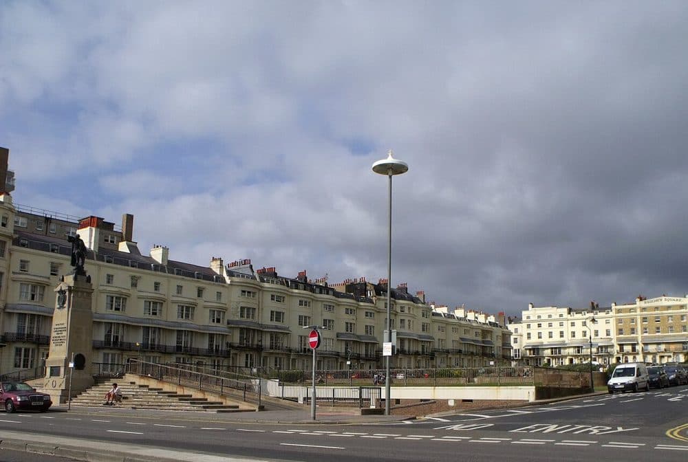 A view along the seafront terraces of Regency Square in Brighton, with cream and white Regency buildings on the right and a road in front under a cloudy sky
