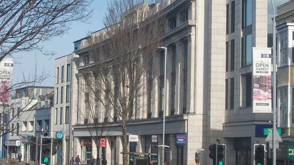 Buildings on London Road in Brighton on a sunny day, with bare trees, traffic lights and an Open Market banner
