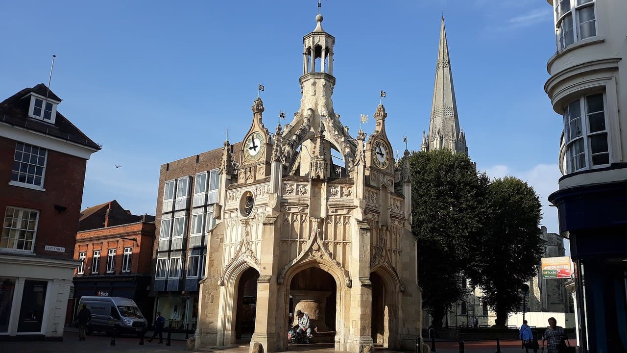 Chichester Market Cross, a stone and carved Gothic structure with two clocks, in a quiet city centre square with the cathedral spire behind