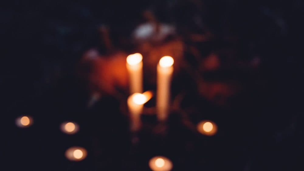 Lit white candles and tealights beside an orange pumpkin on dark ground at night