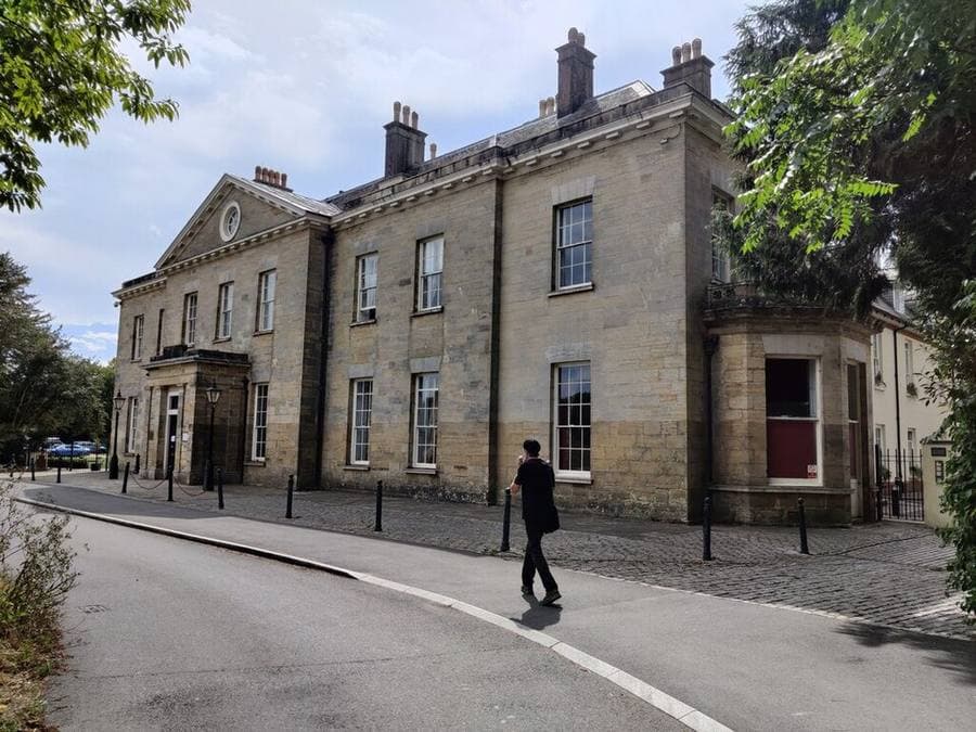 Stanmer House, a pale stone building with a pedimented front and tall chimneys, seen from the road