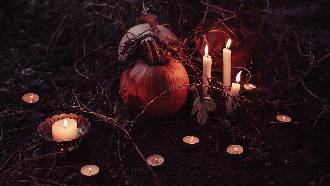 Lit candles glowing among pumpkins on a dark autumn night