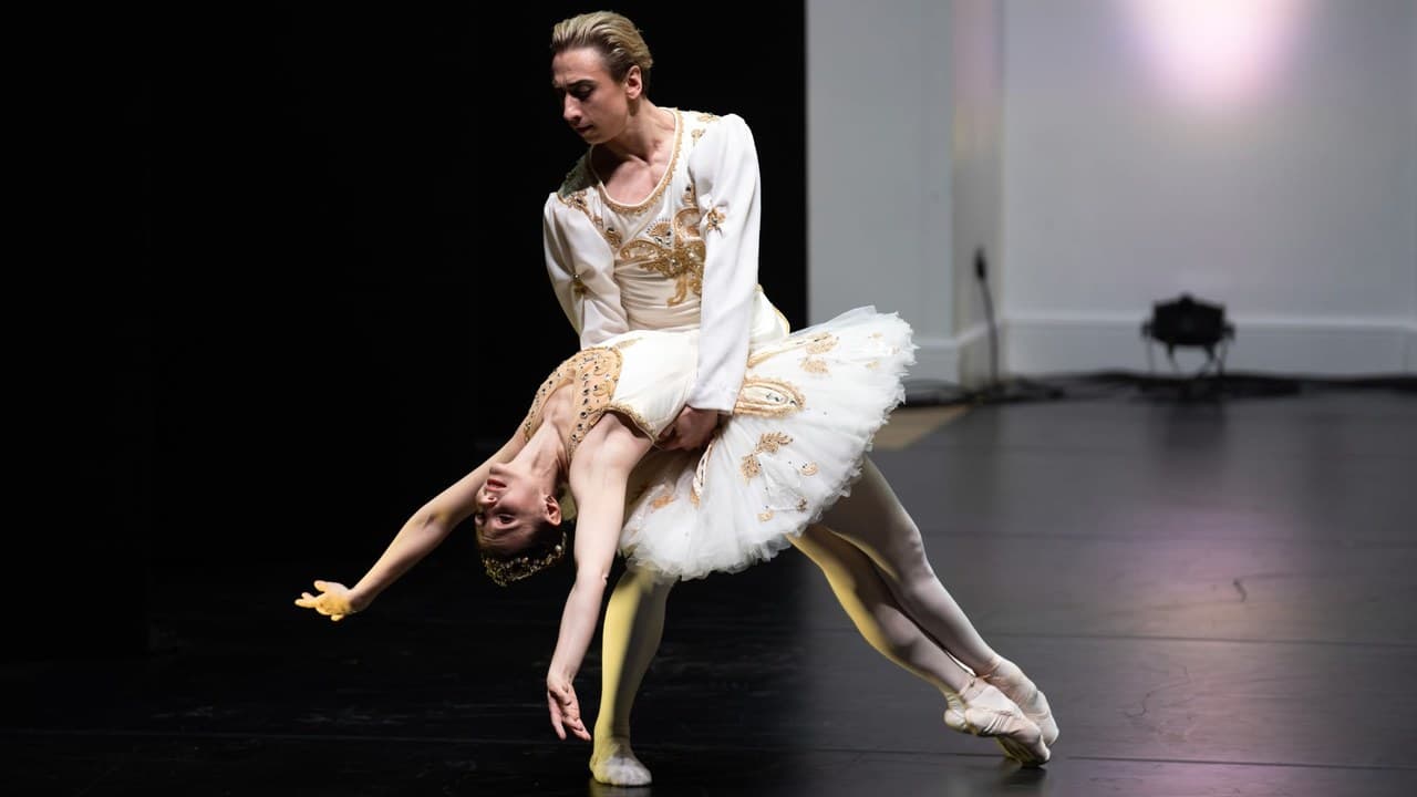 A male and a female ballet dancer in white and gold costumes on a stage, the woman arched backwards in his arms