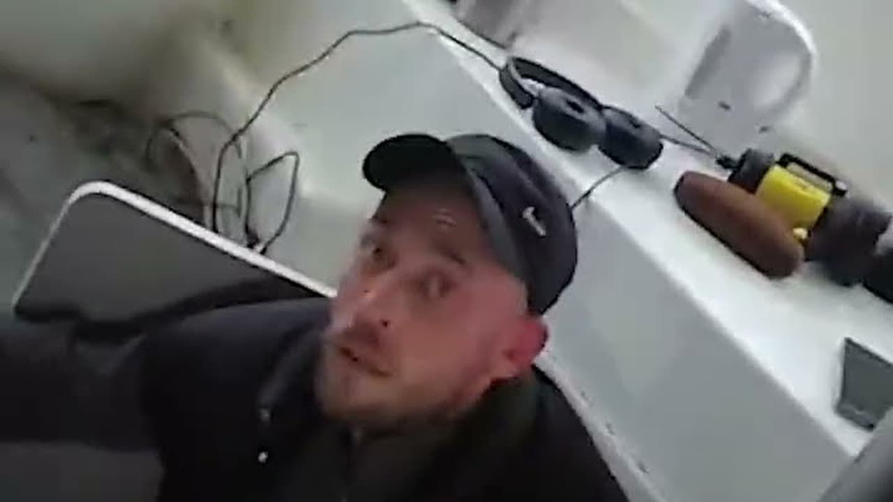 Still from National Crime Agency footage showing a man in a dark cap and jacket inside the cabin of a fishing vessel