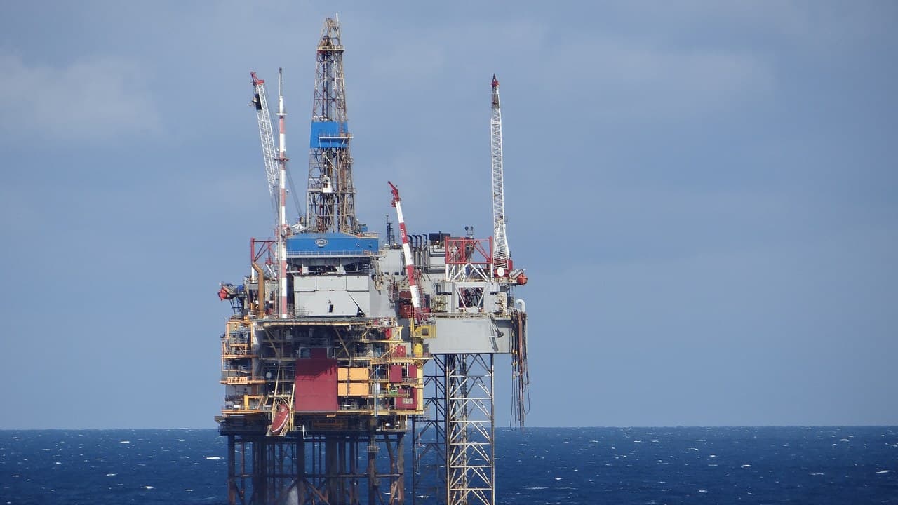 An offshore oil and gas platform with a drilling derrick and cranes standing in a choppy dark blue sea under a grey-blue sky
