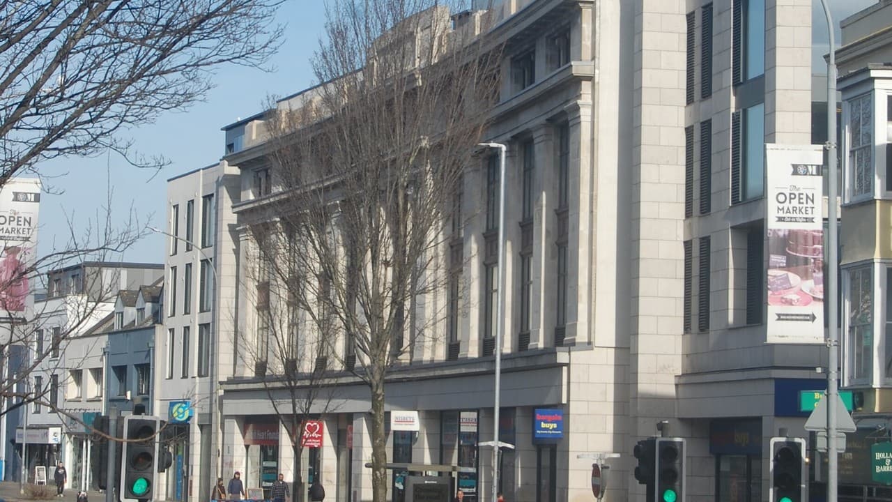 Buildings on London Road in Brighton on a sunny day, with bare trees, traffic lights and an Open Market banner