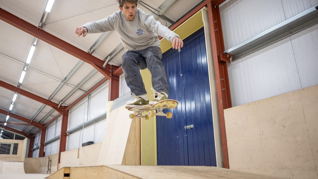 A skateboarder in mid-air above a wooden ramp at The Skate Club indoor skatepark in Hove