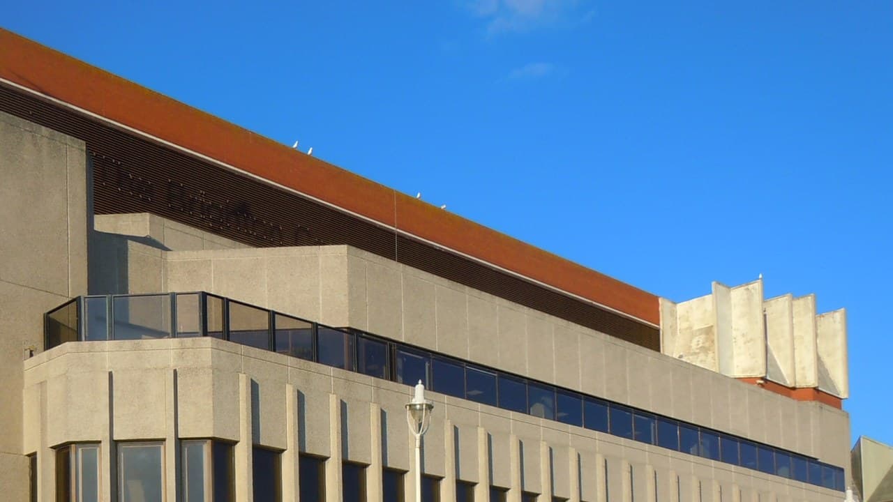 Close view of the upper floors of the Brighton Centre on Kings Road, a concrete and glass building with an orange roofline against a clear blue sky