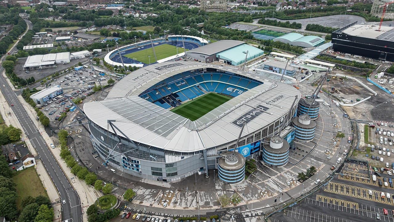 The Etihad Stadium in Manchester seen from above, with the pitch, the curved roof and the athletics track next door